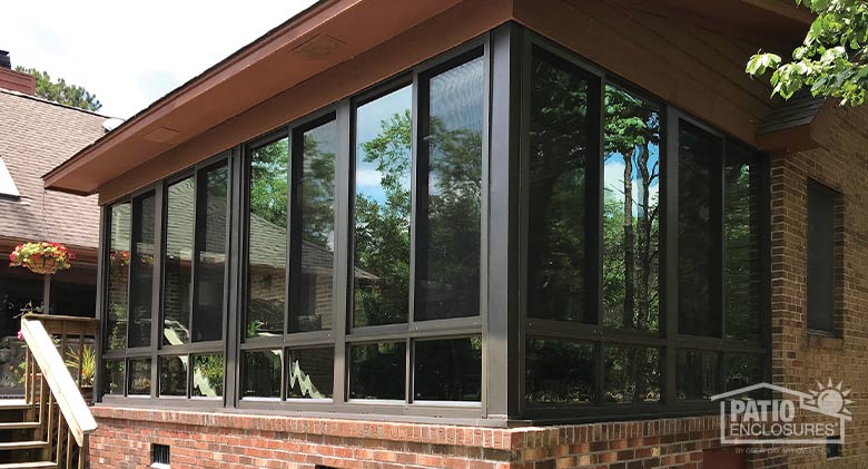 A brown sunroom with glass knee wall on a concrete patio attached to a brick home