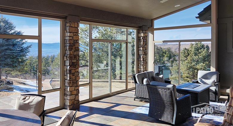 A sunroom patio enclosure with tan frame between stone columns allows sun to stream in for abundant natural light and fabulous views.