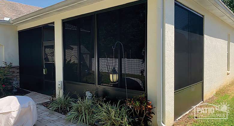  The exterior of a sunroom with soft vinyl windows and solid knee wall in dark brown and a small garden in front.