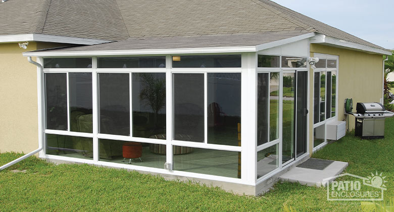 The exterior of a white sunroom with glass knee wall and transoms which enclosed a corner concrete patio.