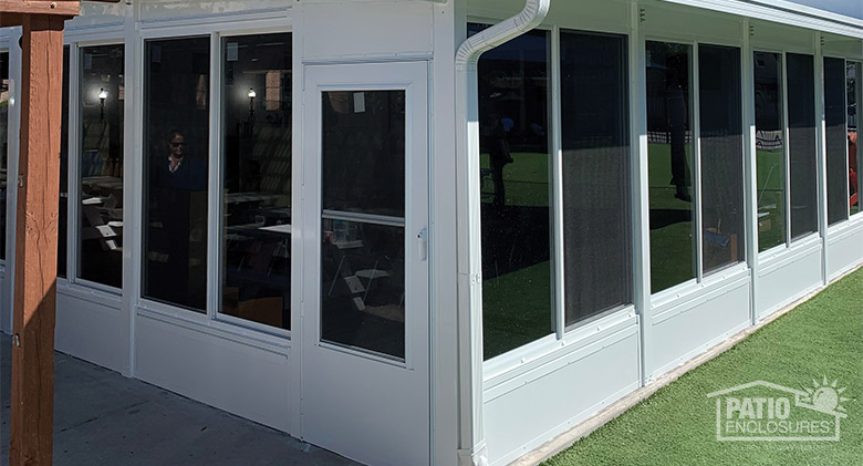 The exterior of a white sunroom with solid knee wall, storm door, and single-sloped roof.