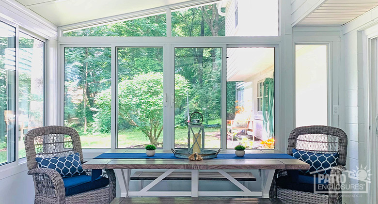The bright interior of a glass sunroom with shed roof focusing on a table with two chairs and two benches and blue accents.