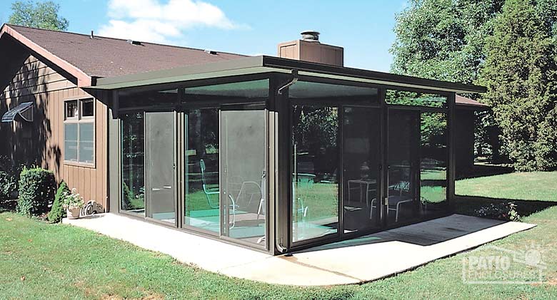 A brown glass sunroom enclosed a concrete patio in the backyard of a one-story home.