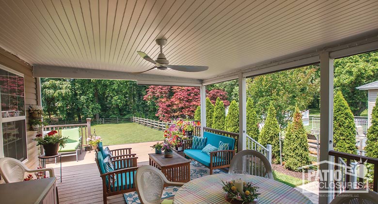 A deck cover with ceiling fan shades a seating area with bright blue cushions as well as a dining table.