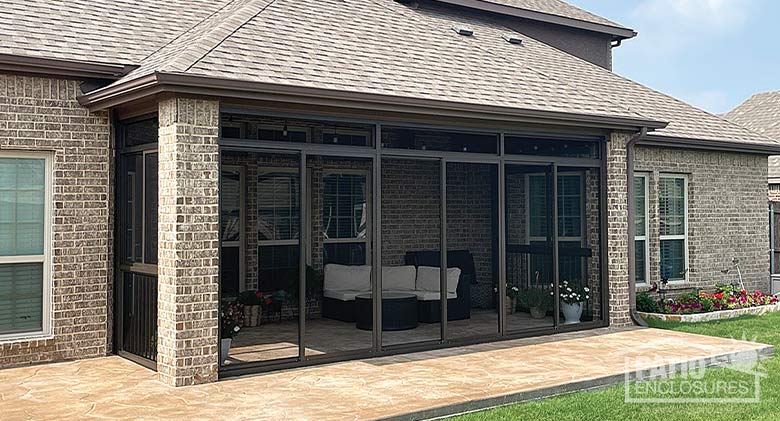 The exterior of a brown-framed screen room enclosing a patio on a brick home.
