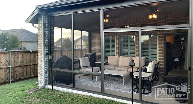 White custhions on black metal furniture make a comfortable seating area inside a brown screen room patio enclosure.