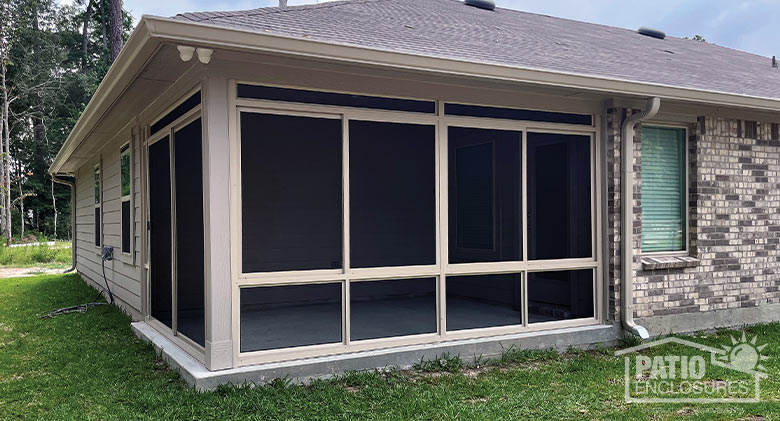 The exterior of a corner patio enclosed with a screen room with beige frame and a screened knee wall and transom.