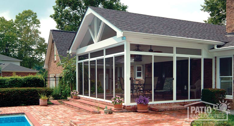A screened patio enclosure with gable roof, floor-to-ceiling sliding doors, and screened transom on an orange brick patio.