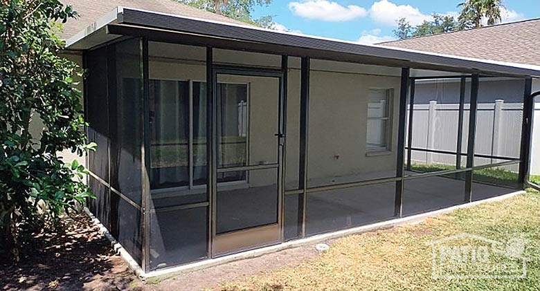 A brown screened room with a solid roof and screen door on a concrete patio.