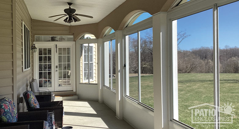 The interior of a screened patio with solid knee wall and scalloped edged on the top; French doors at the end of the room.