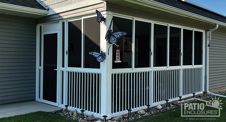 An enclosed corner patio screen room with picket railing, blue butterfly décor on the outside and a bird feeder on hook.