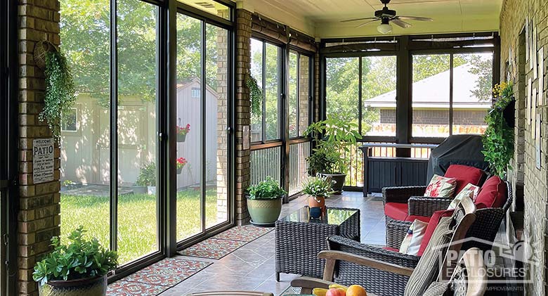 S A brown framed screen room with red cushions on brown wicker chairs, potted plants, and a ceiling fan.