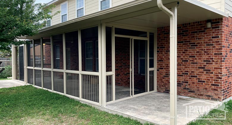 : A beige screen room with a roof extension and picket railing system on a concrete patio.