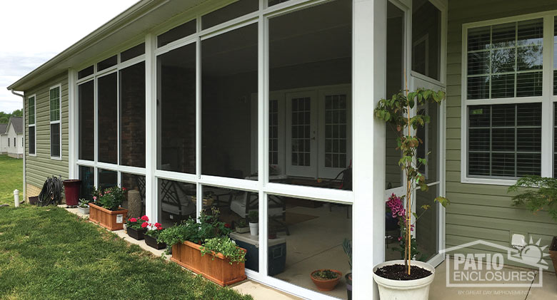 Potted plants and flowers surround a white screen room patio enclosure with screened knee wall and transom.