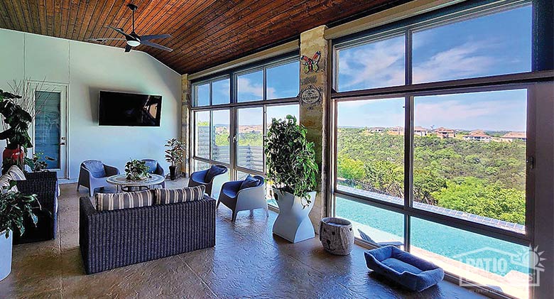 A glassed in lanai with comfortable furnishings, a TV, and a view of an outdoor pool and trees and houses beyond.