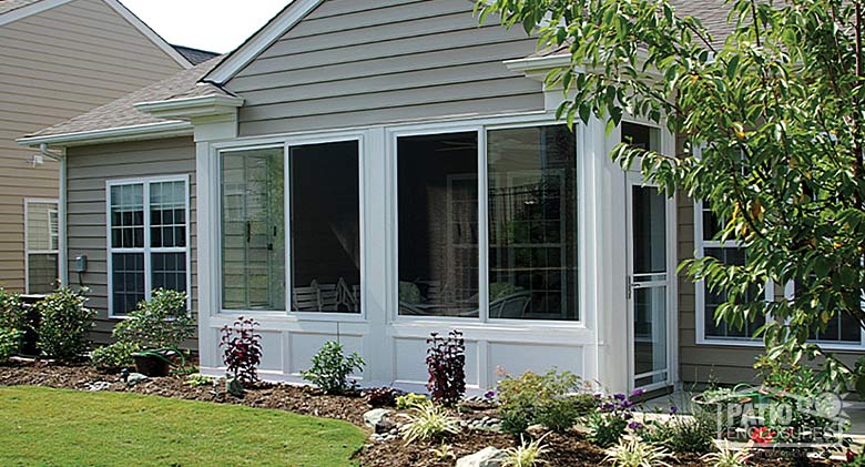 A covered lanai or porch enclosed with glass and solid knee wall with a storm door exit to the patio. Neatly landscaped.