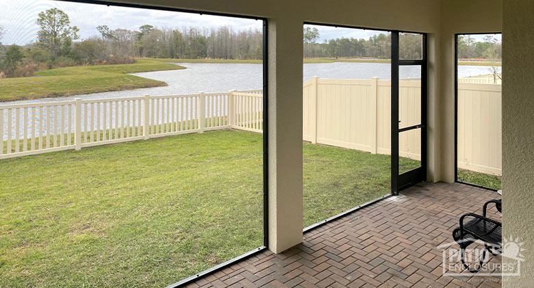 A view of a fence, lake and wooded area from the inside of a screened lanai.