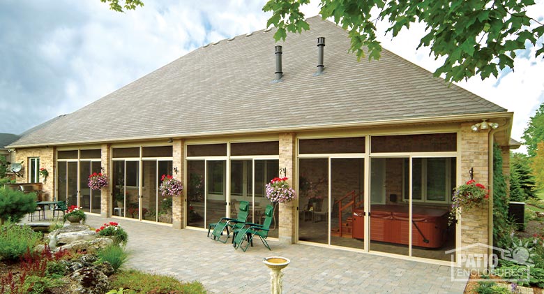 A large porch or screened lanai enclosure opening onto a brick paver patio with hanging flowers and gardens around.