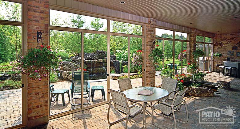 Interior of a large porch or lanai enclosure looking out onto lush gardens and waterfall, decorated with hanging flowers.