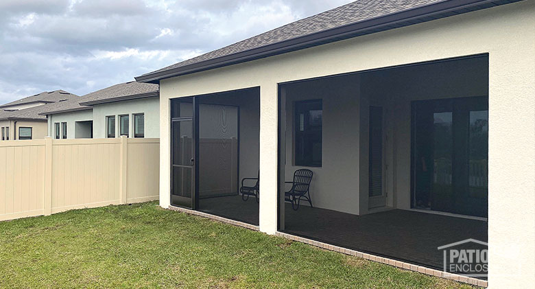 Wall-to-wall screens on a porch or lanai screen enclosure with storm door on a beige stucco home.