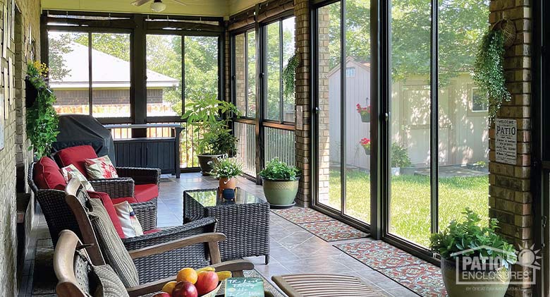 Comfortable wicker furniture with red cushions inside a brown screened lanai enclosure with picket railing system.