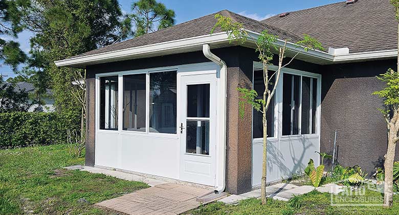 A porch or lanai enclosure of glass with a solid knee wall in white, on a brown stucco house.