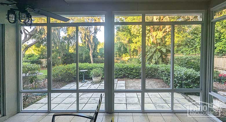 Looking through the glass wall of a lanai enclosure at the gardens and lush landscaping of the backyard.